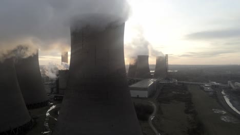 Aerial-view-of-sunrise-emerging-from-behind-UK-power-station-cooling-towers-smoke-steam-emissions