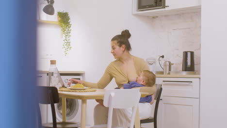 Junge-Mutter,-Die-Mit-Laptop-computer-Arbeitet-Und-Ihr-Baby-Zu-Hause-Stillt-1
