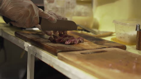 Person-In-Gloves-Chopping-Meat-Into-Cubes-At-The-Kitchen