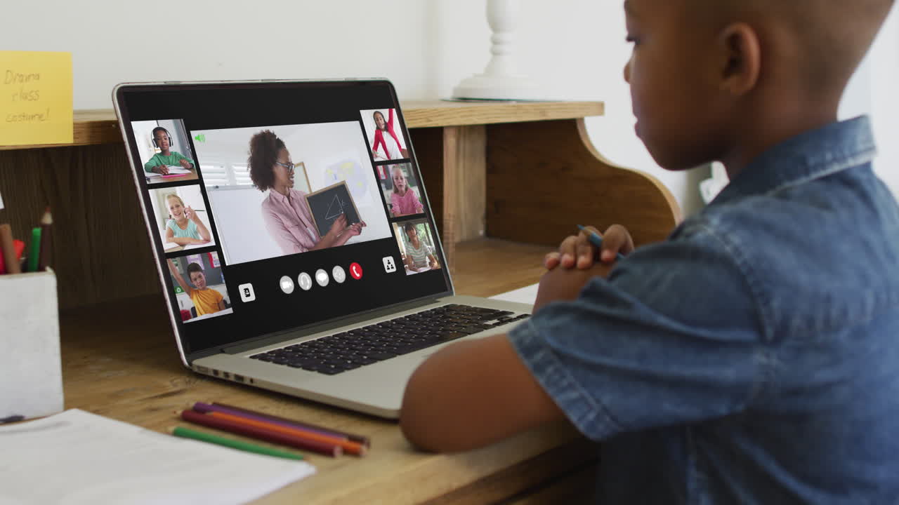 African american boy holding a pencil having a video conference on laptop at home