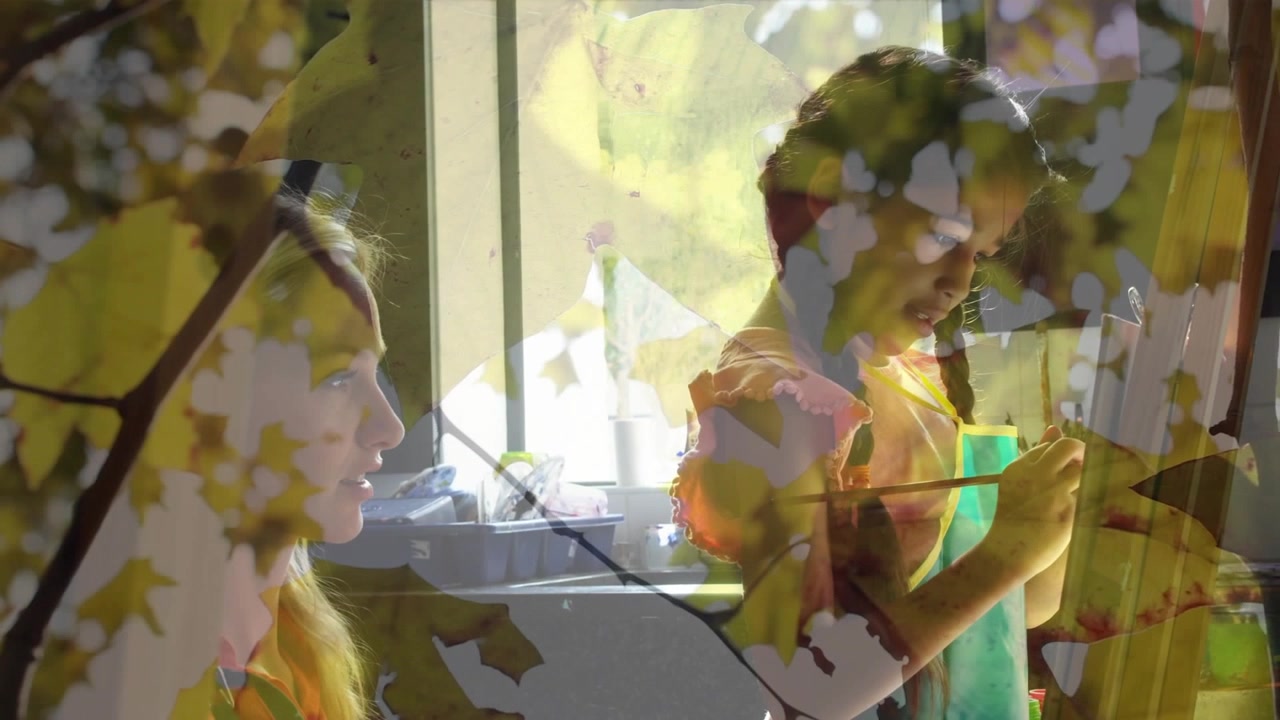 Child raising brush, painting while adult teaching in kitchen, leaf overlay shifting across scene