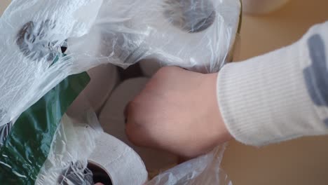 close up of a hand reaching into a plastic bag filled with toilet paper rolls