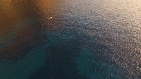 Aerial-view-of-an-electric-surfboarder-riding-through-Spain's-tranquil-waters-at-sunset