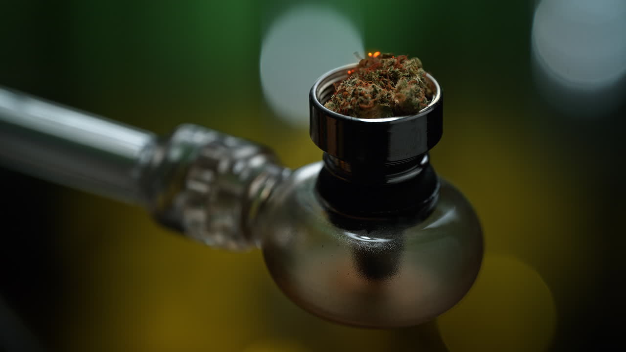 fumando cannabis desde una pipa de vidrio, la marihuana ardiendo en macro y cámara lenta en el fondo verde