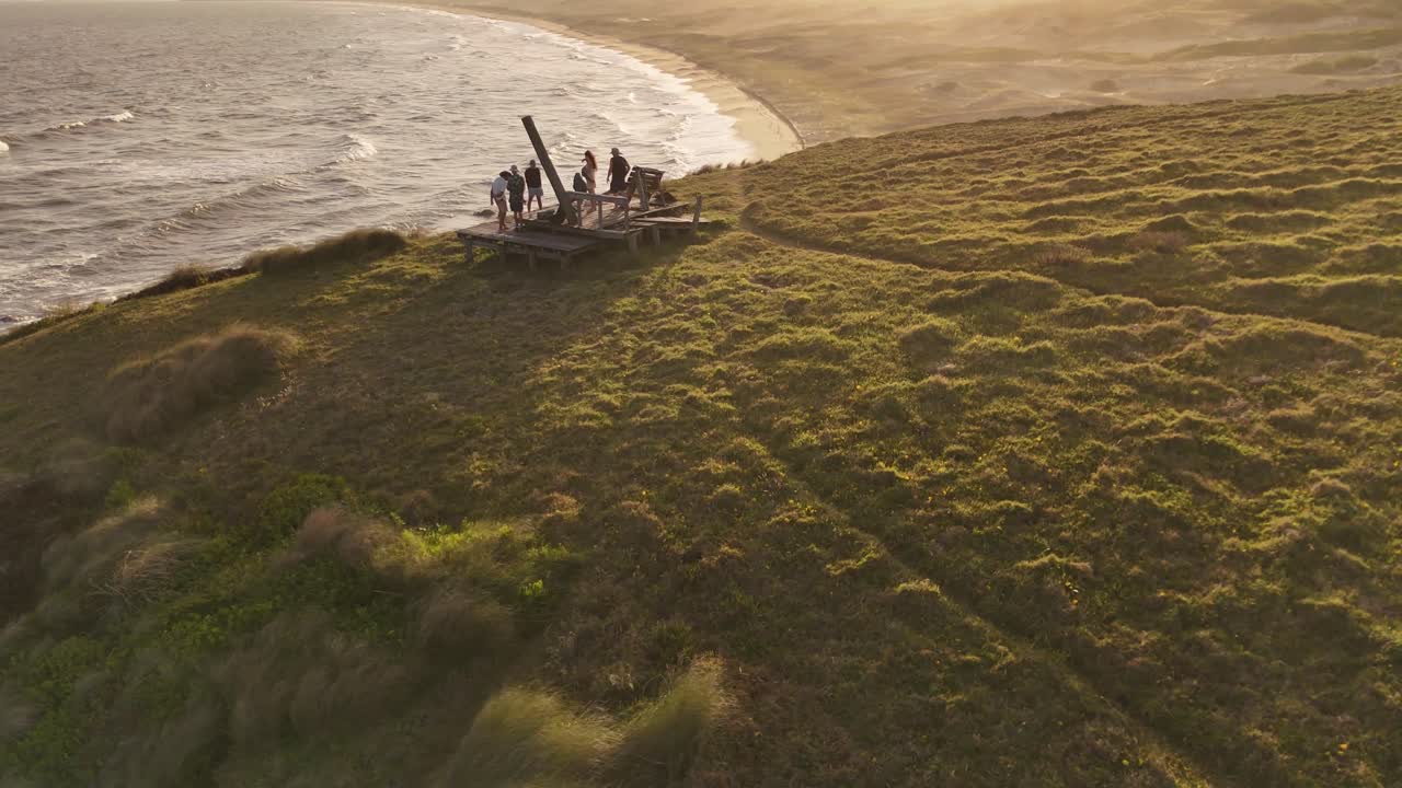Sei amici su un belvedere sul Cerro Chato, si godono la vista di Playa del Barco al tramonto in Uruguay. Ripresa aerea orbitante, slow motion.