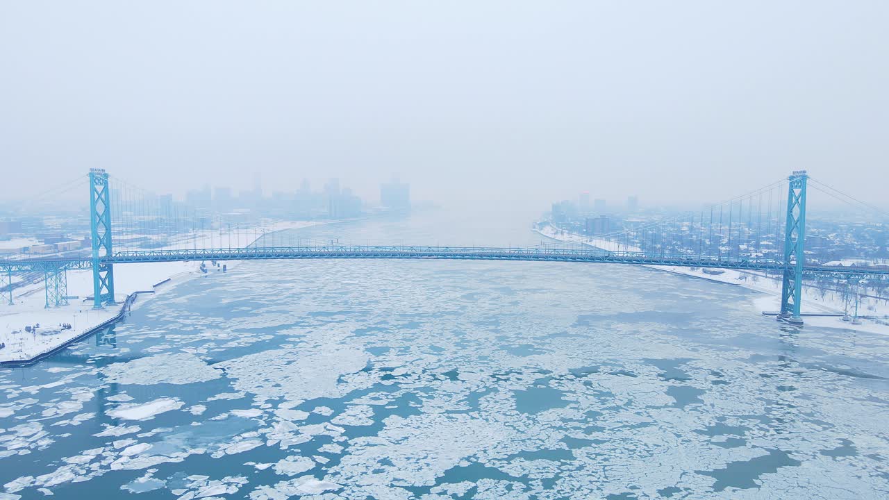 Wide view of Ambassador Bridge crossing icy Detroit river in foggy weather