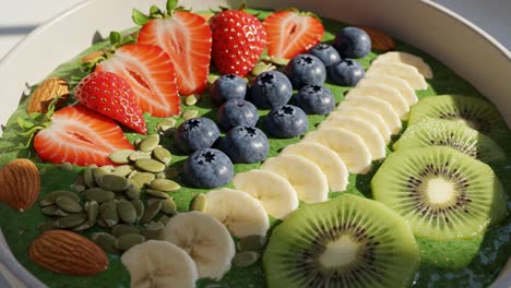 a colorful smoothie bowl topped with fresh fruits and nuts, featuring strawberries, blueberries, bananas, kiwi, and pumpkin seeds for a healthy breakfast delight