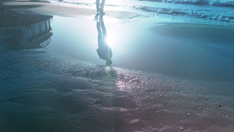 Mans-reflection-steps-over-puddle-and-then-throws-stones-into-sea-during-early-morning-sun