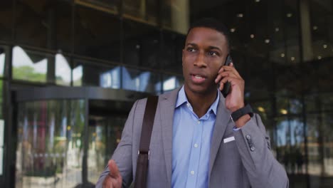 Hombre-De-Negocios-Afroamericano-Hablando-Por-Teléfono-Inteligente-Fuera-Del-Moderno-Edificio-De-Oficinas