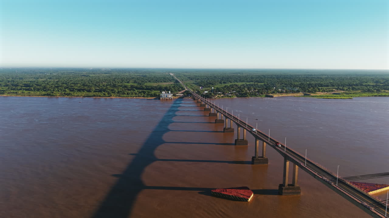 Right tracking drone shot over the General Belgrano Bridge with morning sun casting shadows over the murky river and adjacent green landscape