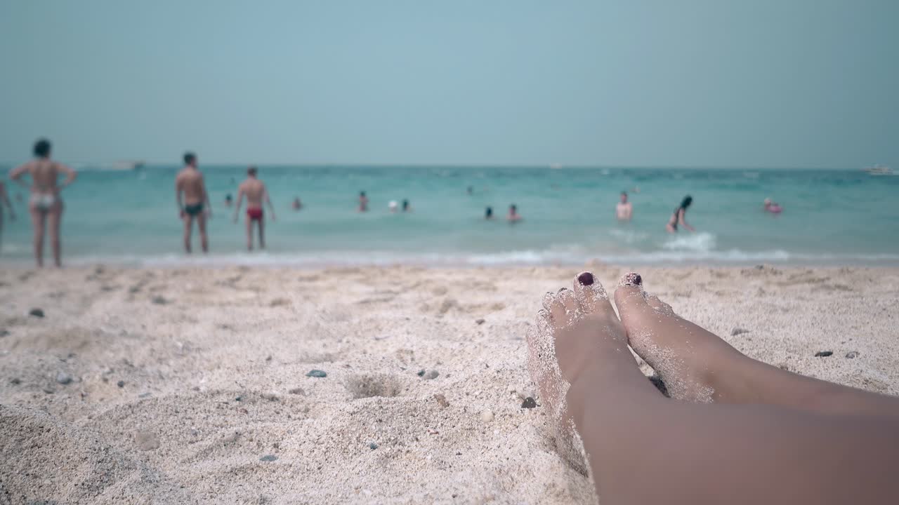 una mujer delgada con pedicura marrón sacude los pies de la arena