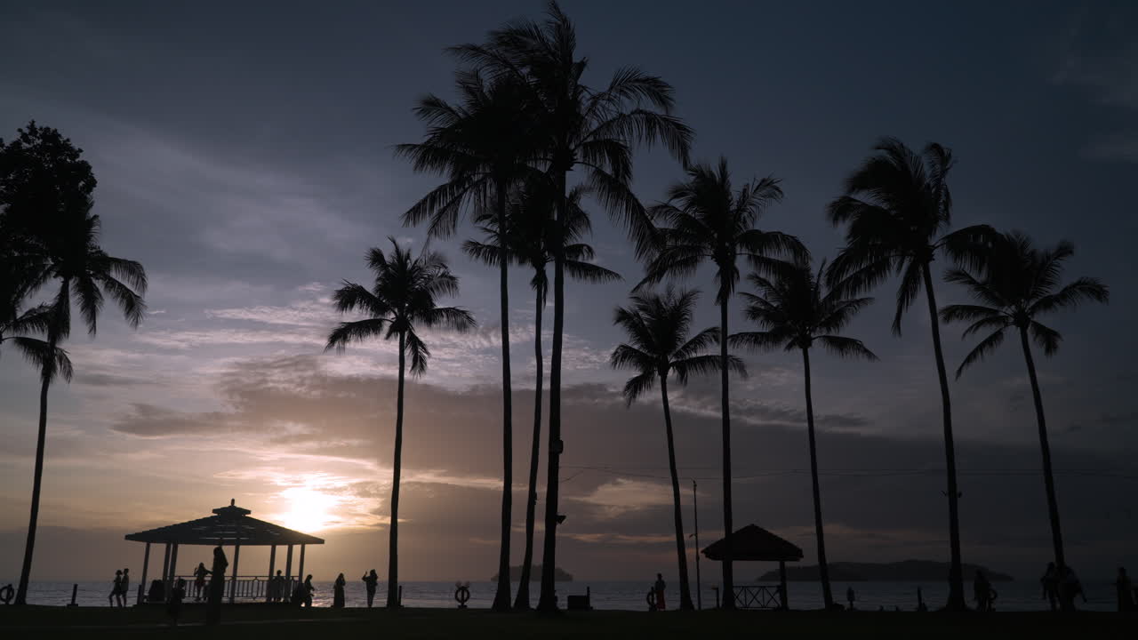 탄중아루 해변 - 코코넛 야자나무의 실루엣과 말레이시아 코타키나발루에서 장엄한 화려한 일몰을 즐기는 사람들