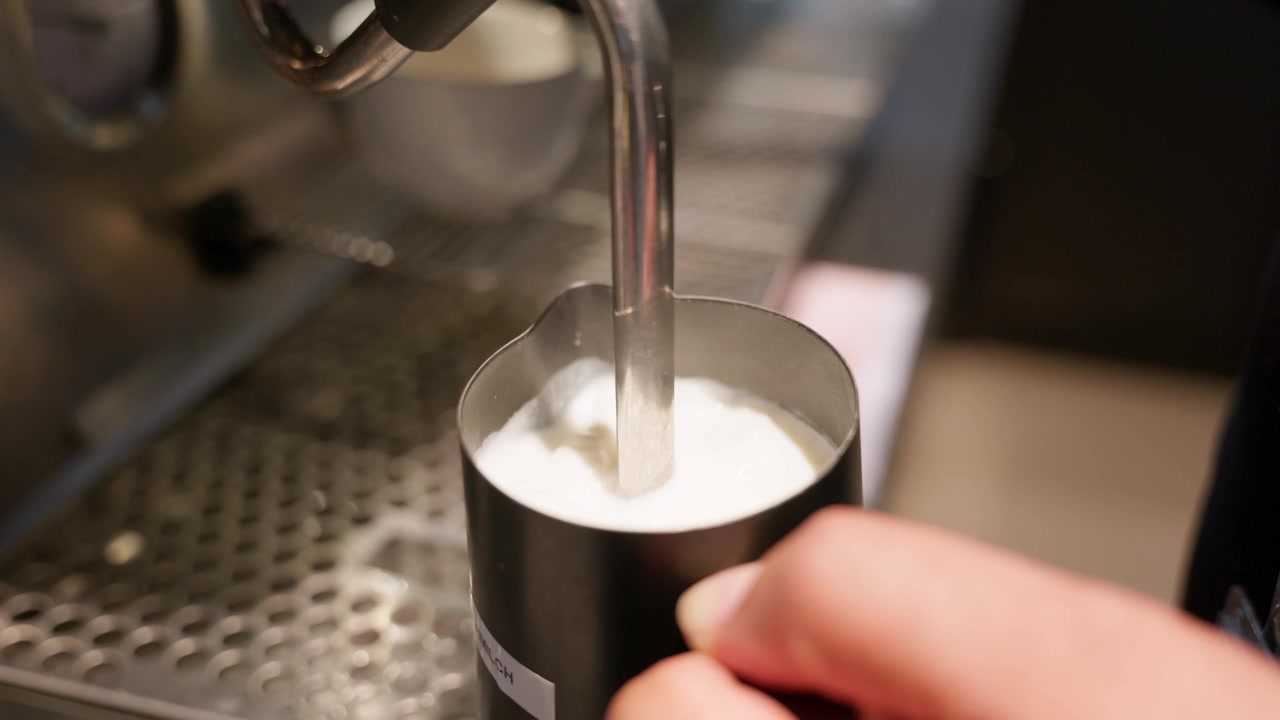 Primo piano, barista che monta il latte con una macchina da caffè espresso professionale mentre prepara una bevanda al caffè speciale. Ideale per temi di caffè, ospitalità, servizi e industria alimentare