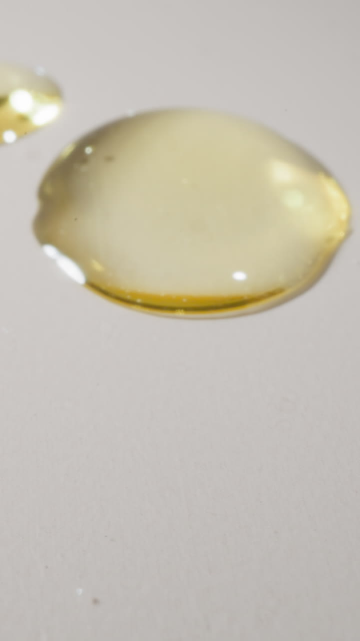 Golden drops of jojoba oil falling on white plain surface. Component for professional skincare cosmetic products presented for sale macro