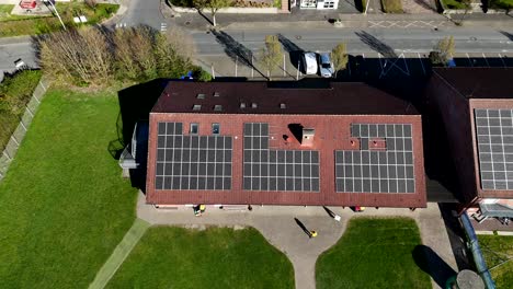 solar panels on red tile roof of apartment building. sunny day in spring season with green grass. aerial top down shot. renewable energy production during bright sunlight.