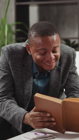 african-american man tutor laughs reading task in textbook with junior boy student at private english language lesson with native speaker slow motion
