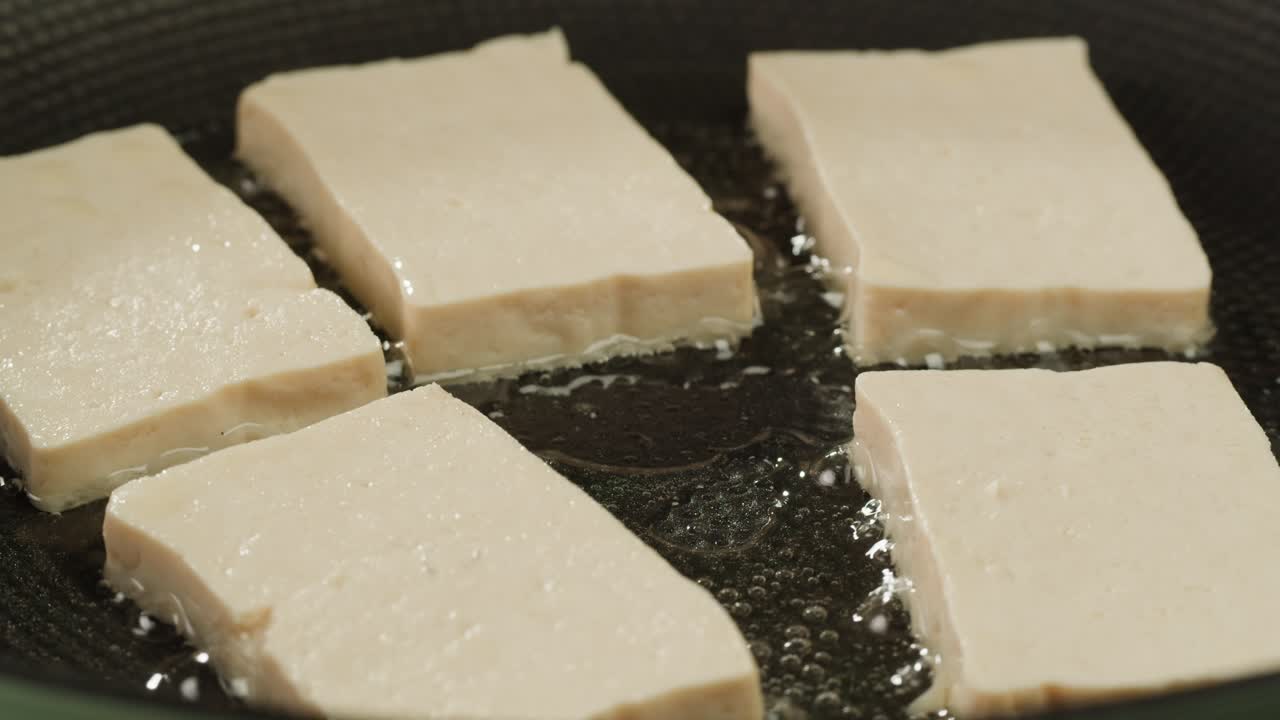 Fried tofu with sesame seeds and spices on cast iron pan, cooking japanese salad. Healthy ingredient for cooking vegan vegetarian diet food. Roasted tofu over black background.