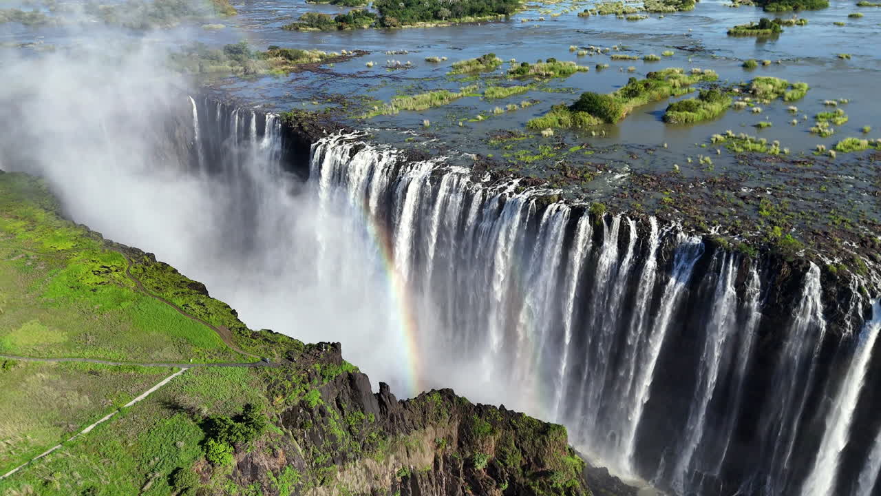 Aerial view of Victoria Falls with powerful waterfall plunging into gorge, mist rising above lush green forest, dramatic natural wonder and iconic travel destination in Africa