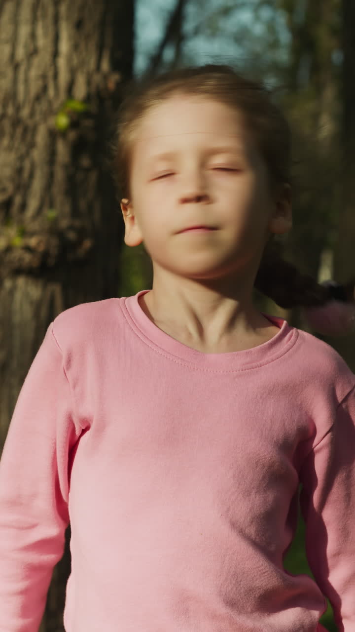 Funny little girl shakes head and waves stick in spring park closeup. Joyful child has fun grimacing in green garden. Active playing outdoor