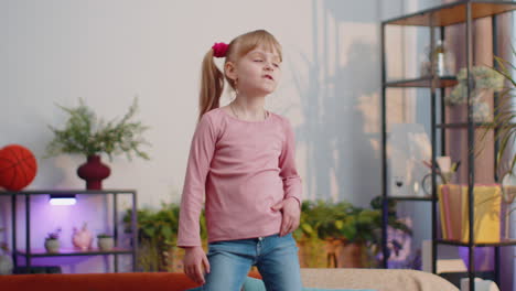 happy child girl kid in headphones dancing and jumping while listening to the music at home alone