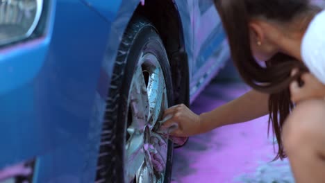 woman washing a car wheel with sponge