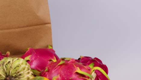 a hand places cherimoya and dragon fruits into a paper bag, showcasing vibrant tropical produce.