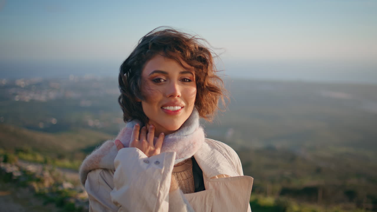 Primo piano di una ragazza allegra che sorride in cima a una collina sotto la luce del sole suggestiva. Esploratrice felice che si gode il momento.