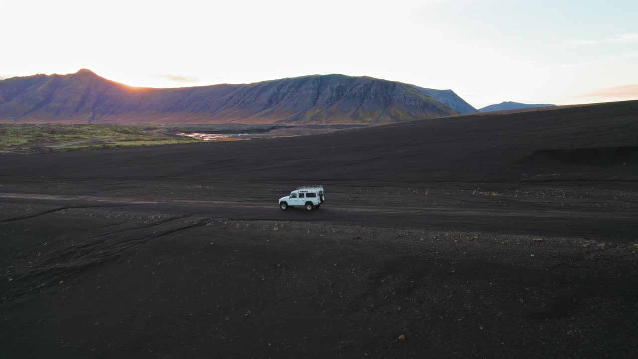 defensor de land rover blanco conduciendo en el paisaje islandés de arena negra durante la puesta de sol, disparo aéreo de drones