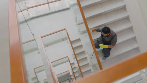 vista superior de un hombre de limpieza árabe con guantes limpiando barandillas de escaleras y cristales dentro de un edificio de oficinas 1