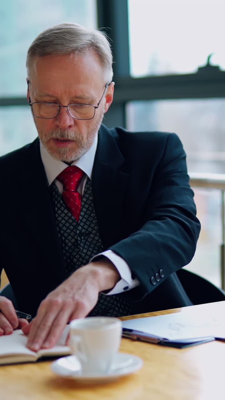 Smart mature businessman working in the office. Senior man in elegant suit sitting at the desk and using notebook in his work. Business concept. Vertical video