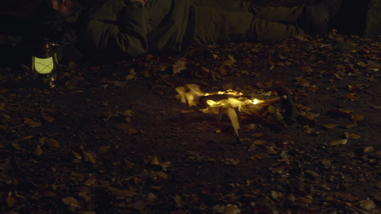 Man Sleeping by Campfire in Forest at Night