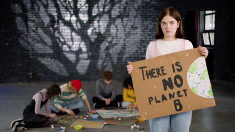 serious young environmental activist holding a cardboard with there is no planet b" inscription and looking at the camera"