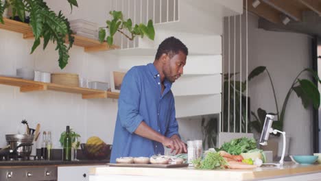 Happy-african-american-man-cooking-dinner-in-kitchen,-using-tablet