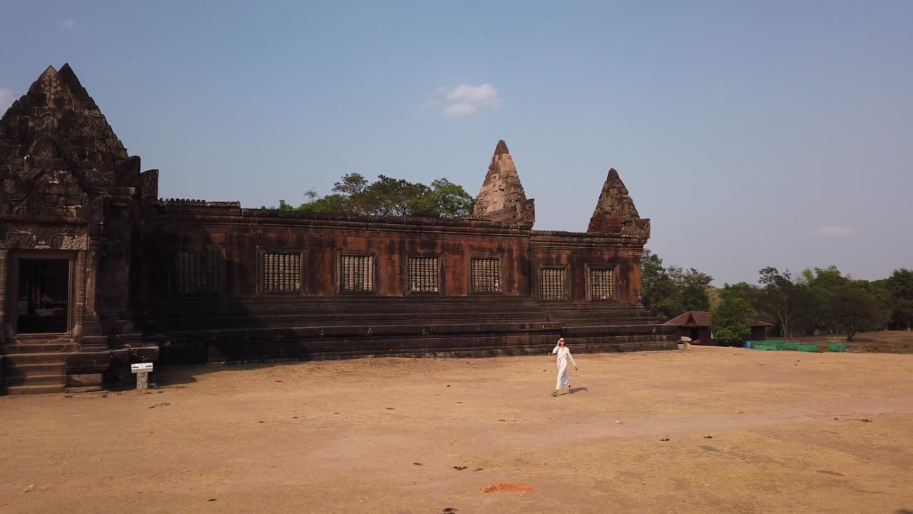 긴  드레스와 선글라스를 입은 아름다운 젊은 여성이 wat phou의 크메르 궁전 근처에서 고 있습니다. 힌두 사원 단지. 파사크, 라오스, 아시아. 빛. 고대 문화. 느린 종교 건축.