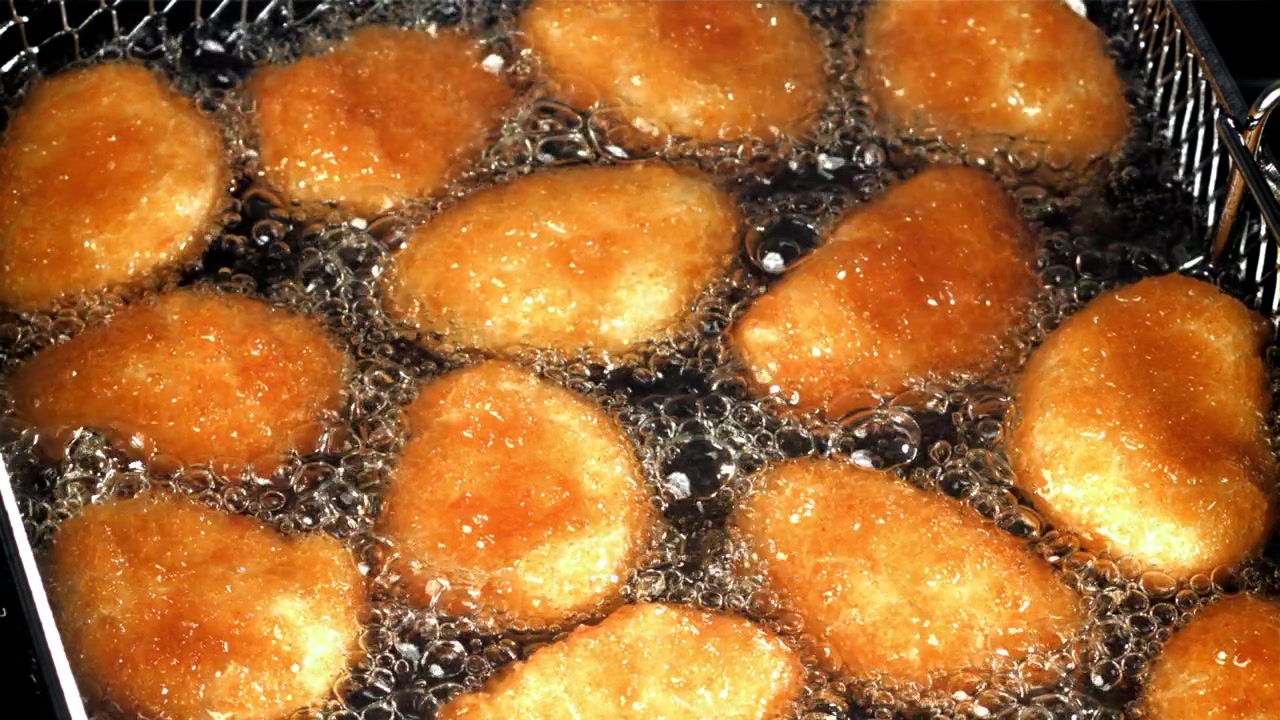 熱い泡立つ油で揚がる黄金色のチキンナゲット