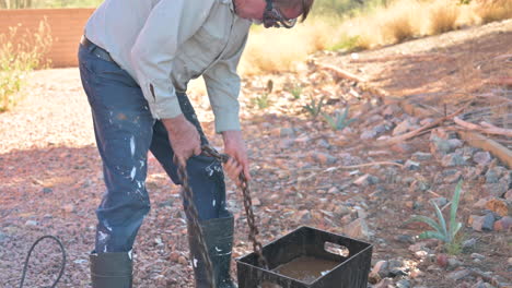 el trabajador masculino limpia la cadena de metal en un balde con agua al aire libre, acerca el zoom