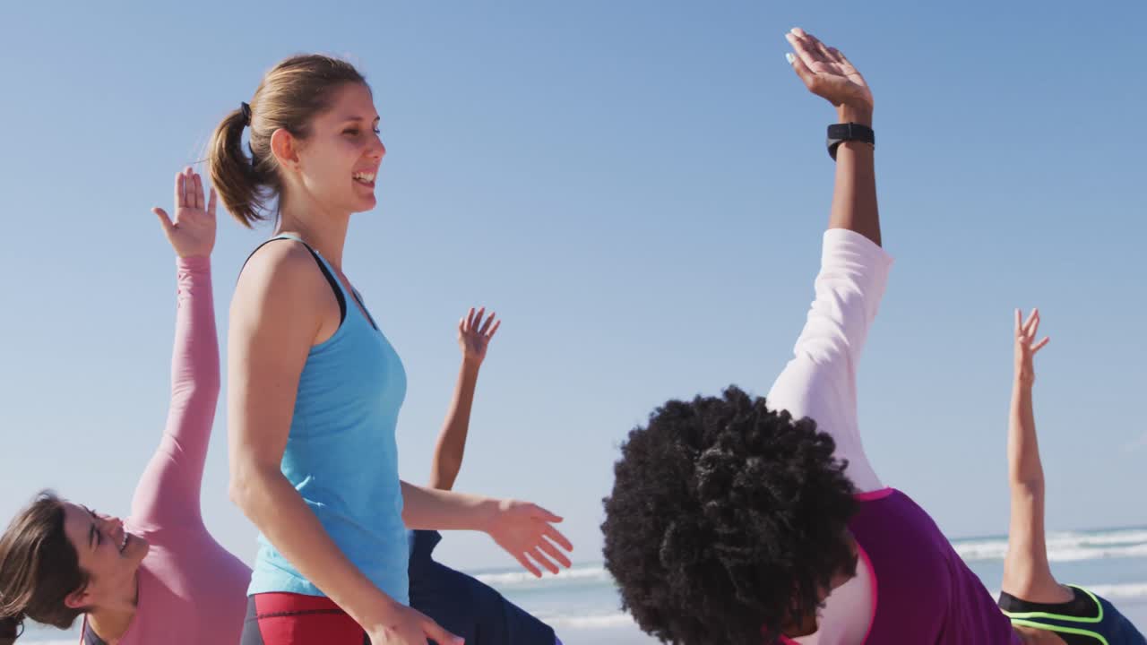 코카시안 요가 선생님 여성이 해변과 파란 하늘 배경에서 여성을 돕고 있습니다.