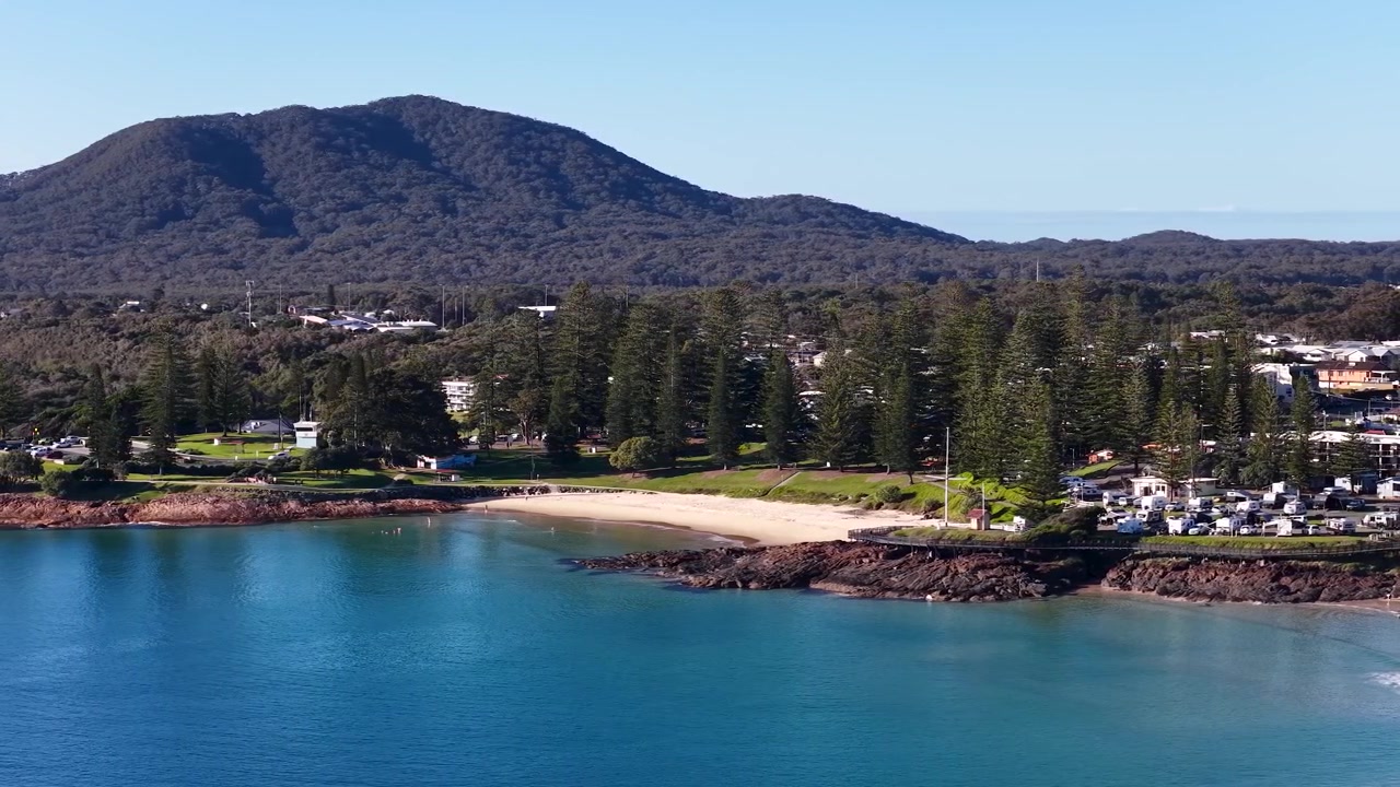 Vidt luftfoto av turkist vann, furutrær og fjell i South West Rocks, Australia