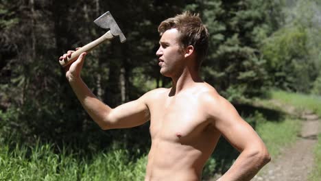 shot of a shirtless man practicing his axe throwing skill by trying to throw his hatchet at a pine tree-1