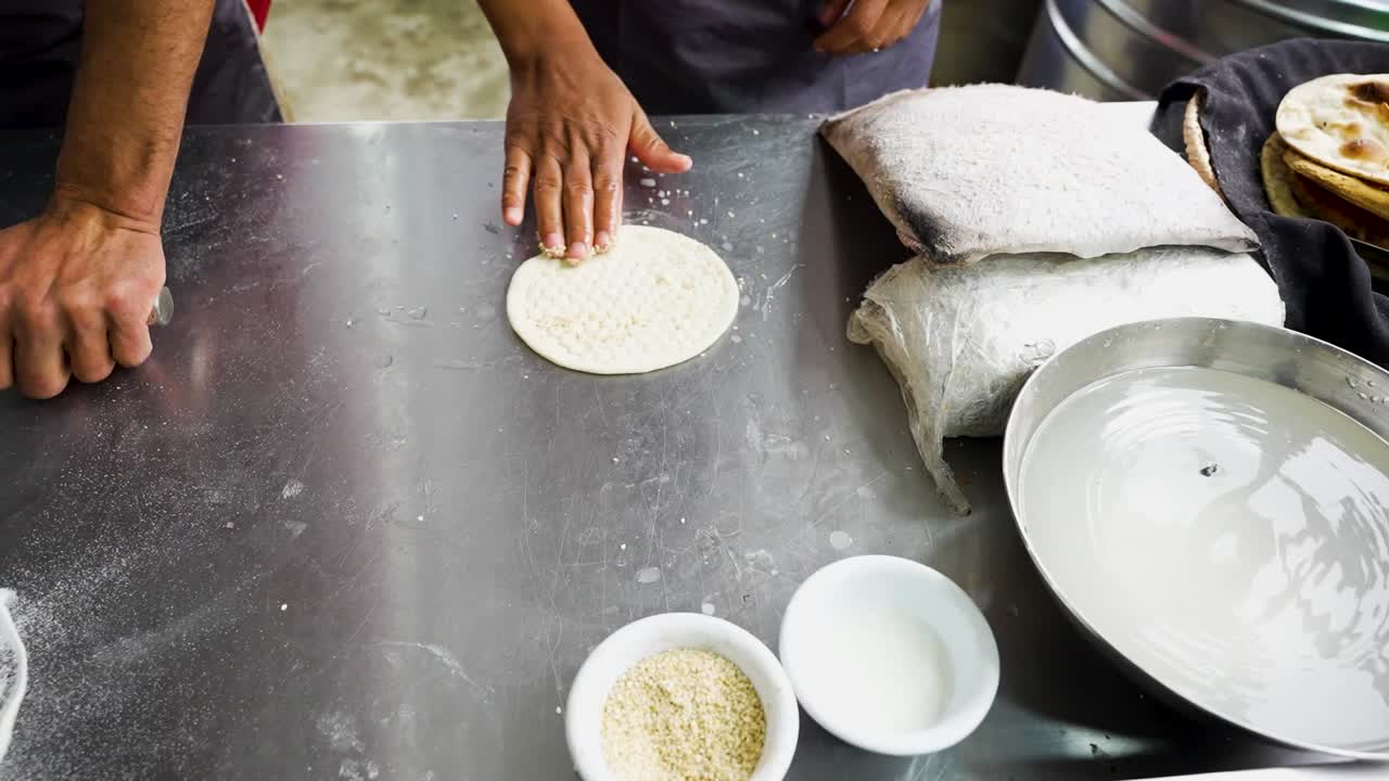 Cook applies sesame and water on naan dough before baking at a Pakistani restaurant