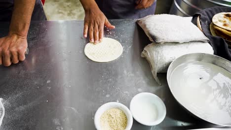 cook applies sesame and water on naan dough before baking at a pakistani restaurant