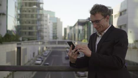 Good-looking-man-leaning-on-banister,-texting-on-tablet,-swiping