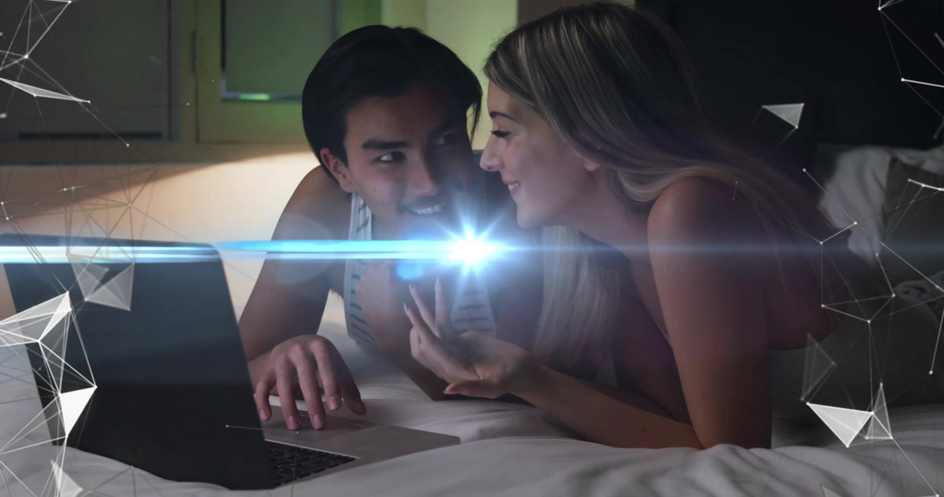 Mujer señalando y hombre usando el portátil en la cama, con una superposición tecnológica que se ilumina y provoca sonrisas compartidas.