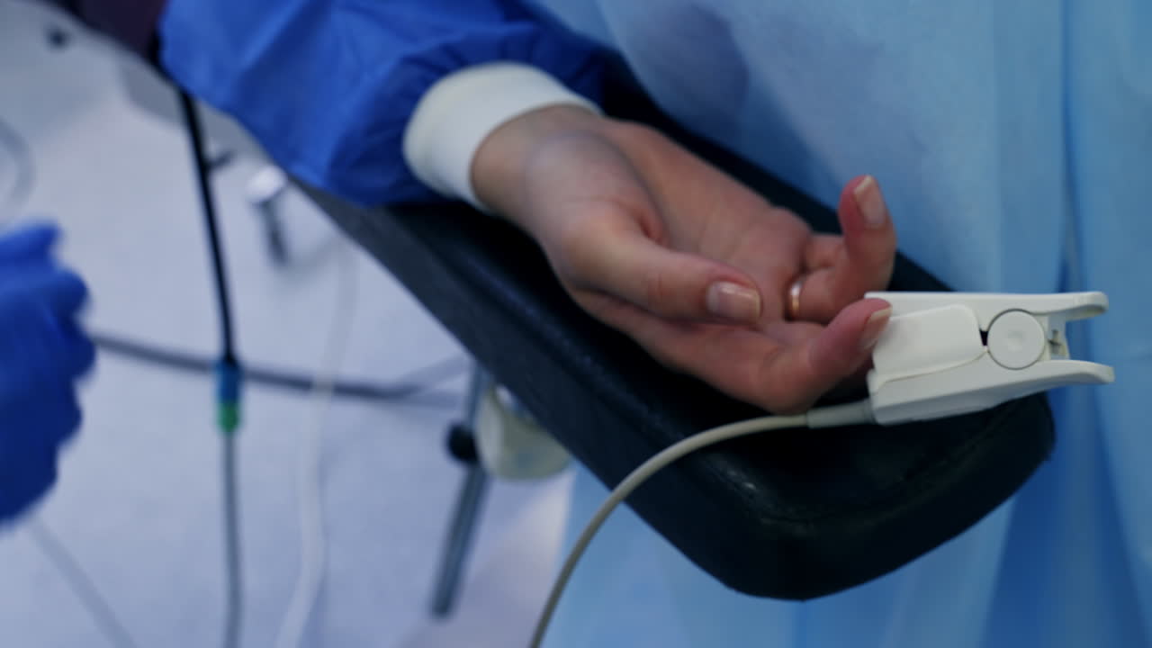 Nurse's hands in blue latex gloves put a sensor on female hand. Close up. Medic places patient's hand in the middle of the hand rest.