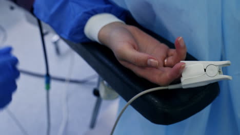 nurse's hands in blue latex gloves put a sensor on female hand. close up. medic places patient's hand in the middle of the hand rest.