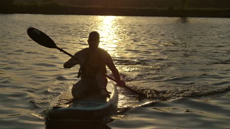 man paddle board seated in deep sunset on lake slomo closeup