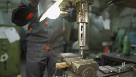 drill bit in motion on a metal part with a workshop worker guiding the process