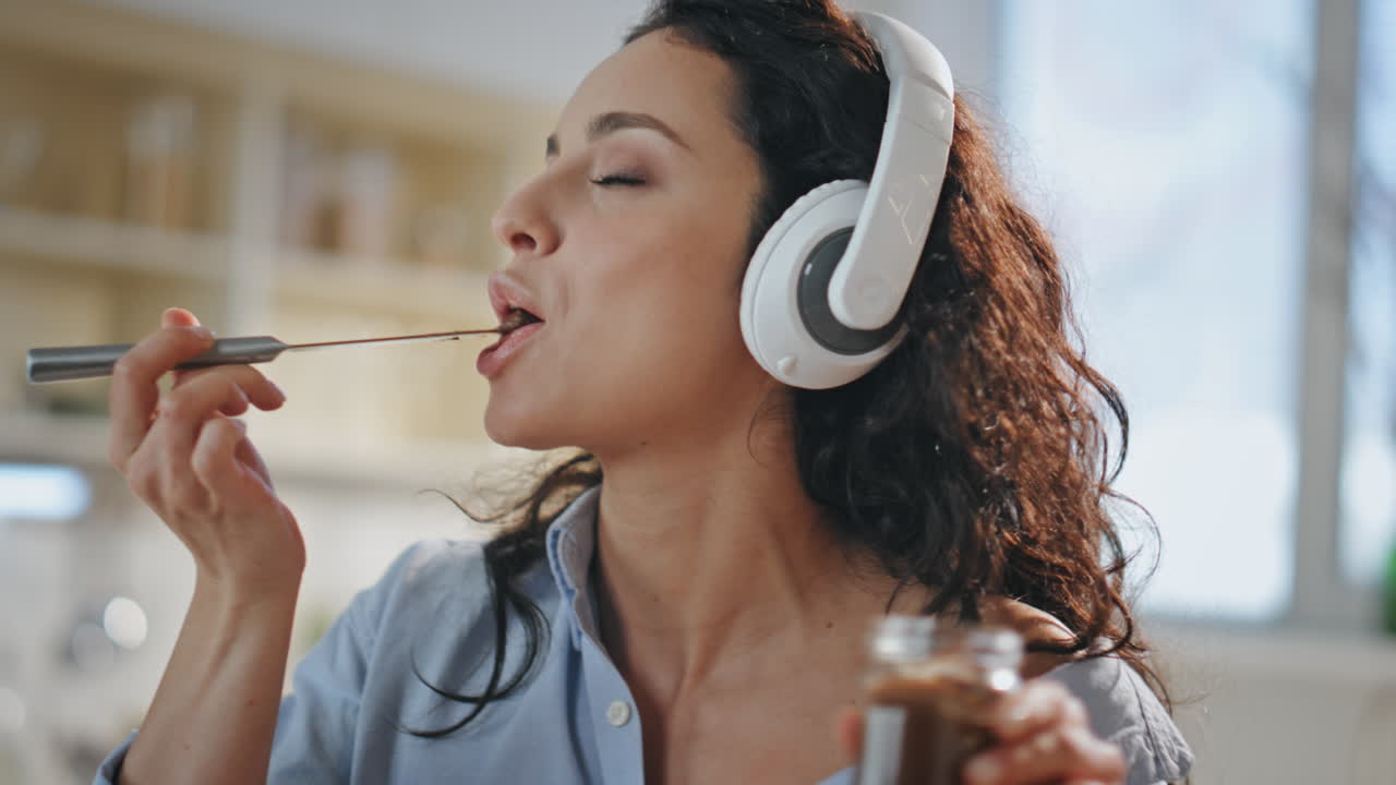 Kochende Frau hört Musik mit Kopfhörern in der Küche Nahaufnahme. Mädchen probiert Essen.