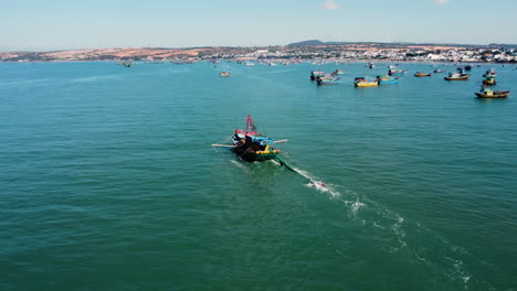 aerial, trawler boat dragging net behind while sailing close to harbor coast