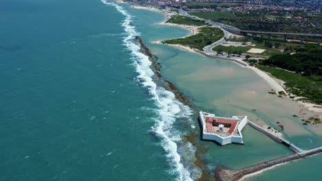 Tilt-up-aerial-drone-wide-shot-of-the-historic-star-shaped-Reis-Magos-fort-built-on-a-reef-with-the-coastal-capital-city-of-Natal-in-Rio-Grande-do-Norte,-Brazil-in-the-background-on-a-warm-summer-day